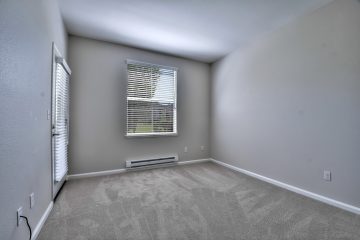 Bedroom with grey walls, carpeting, window, and door to balcony.