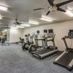 Fitness center with ceiling fans, fluorescent lights, and gym equipment.