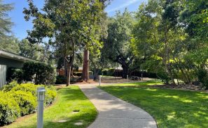 Los Altos Gardens outdoor walkway through grass, bushes, & trees.