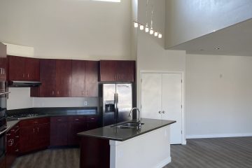 Open floor kitchen with island, dark wood cabinets, stainless steel appliances, & overhead lighting.