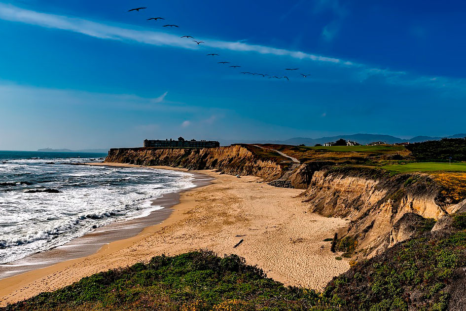 Birds fly across the sky over the beach of Half Moon Bay in California.