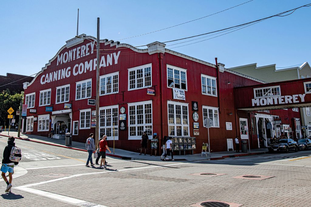 Tourists walk down the street in front of the Monterey Canning Company building while enjoying a day trip to Monterey, CA.