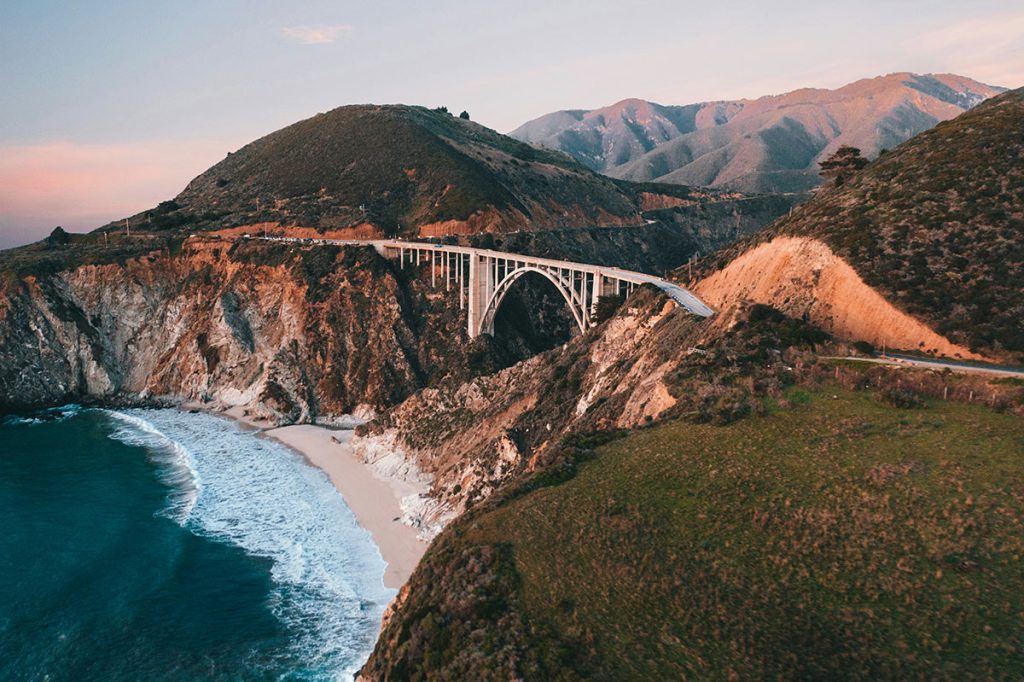 A white bridge connects two steep hillsides along the ocean at Big Sur, CA.