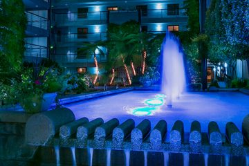 The Cupertino Hotel & Residences outdoor courtyard with water feature and ambient lighting at night is an alluring and calm scene.
